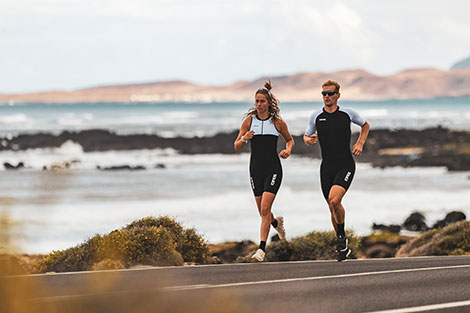 man-en-vrouw-rennend-in-triathlonpak-over-de-weg-langs-de-zee.jpg