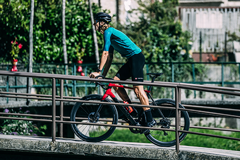 man-fietsend-door-stad-over-een-brug-in-korte-fietsbroek-zonder-bretels-en-in-fietsshirt.jpg