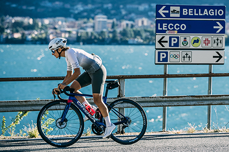 man-fietsend-in-korte-fietsbroek-met-bretels-en-fietsshirt-langs-een-meer.jpg